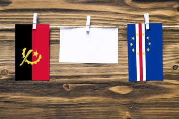 Hanging flags of Angola and Cape Verde attached to rope with clothes pins with copy space on white note paper on wooden background.Diplomatic relations between countries.