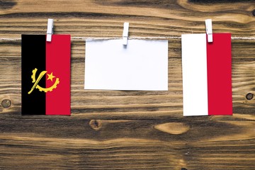Hanging flags of Angola and Indonesia attached to rope with clothes pins with copy space on white...