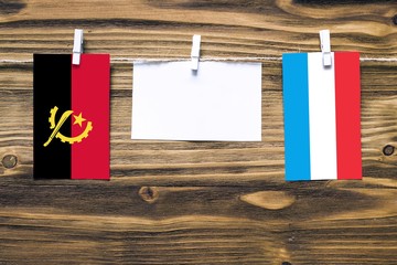 Hanging flags of Angola and Luxembourg attached to rope with clothes pins with copy space on white...