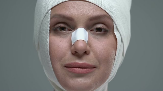 Woman in elastic bandage on face opening eyes, enjoying plastic surgery result