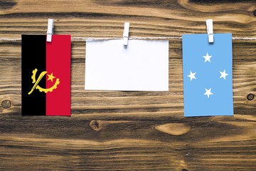 Hanging flags of Angola and Micronesia attached to rope with clothes pins with copy space on white...