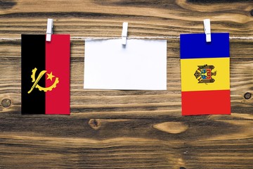 Hanging flags of Angola and Moldova attached to rope with clothes pins with copy space on white...