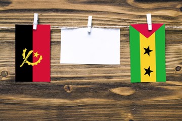 Hanging flags of Angola and Sao Tome And Principe attached to rope with clothes pins with copy space on white note paper on wooden background.Diplomatic relations between countries.