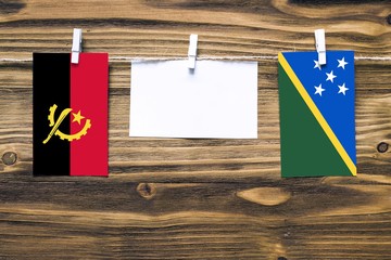 Hanging flags of Angola and Solomon Islands attached to rope with clothes pins with copy space on...