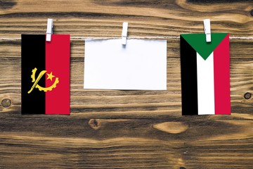 Hanging flags of Angola and Sudan attached to rope with clothes pins with copy space on white note...