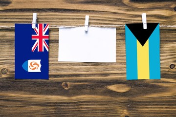 Hanging flags of Anguilla and Bahamas attached to rope with clothes pins with copy space on white note paper on wooden background.Diplomatic relations between countries.