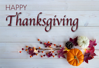 Happy Thanksgiving lettering on white wood background with orange pumpkin, white pumpkin and purple maple leaves