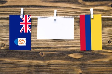 Hanging flags of Anguilla and Colombia attached to rope with clothes pins with copy space on white note paper on wooden background.Diplomatic relations between countries.