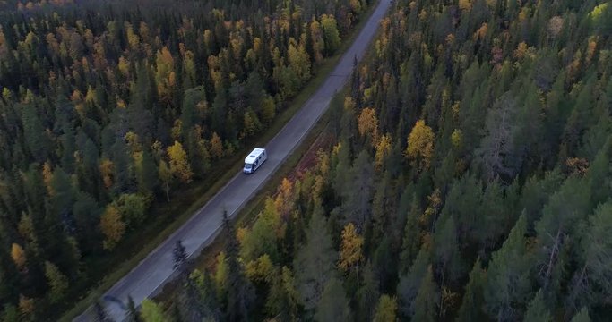 Caravan on a forest road, Aerial, reverse, drone shot, following a camper rv, driving on a route, at lake Jerisjarvi, fall colored trees, on a cloudy, autumn day, in Pallas-Yllas park, Finland