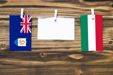 Hanging flags of Anguilla and Hungary attached to rope with clothes pins with copy space on white note paper on wooden background.Diplomatic relations between countries.