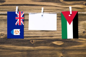 Hanging flags of Anguilla and Jordan attached to rope with clothes pins with copy space on white note paper on wooden background.Diplomatic relations between countries.