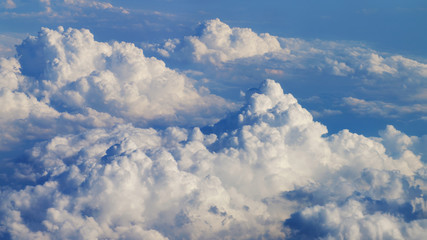Flying over heavenly beautiful cloudscape. Picturesque panorama of dense fluffy clouds softly lit by the sun, moving from right to left on the clear blue sky. View from the airplane window.