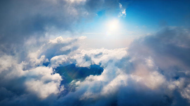 Flying through heavenly beautiful sunny cloudscape. Amazing of white fluffy clouds moving softly on the sky and the sun shining above the clouds with beautiful rays and lens flare.