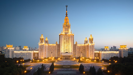 Motion of Moscow State University in the evening, aerial view. Camera moving towards MSU, showing also its alleys and outdoor lighting gradually turning on.
