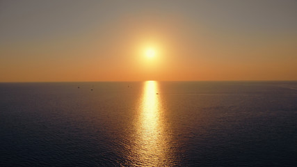 Beautiful aerial panorama of the sunset sea. Picturesque view to the sun going down over the sea, leaving a light path over the water, and the boat crossing the light path in front of the sun.