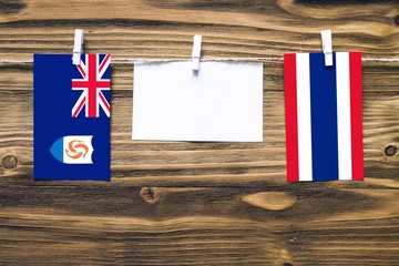 Hanging flags of Anguilla and Thailand attached to rope with clothes pins with copy space on white note paper on wooden background.Diplomatic relations between countries.