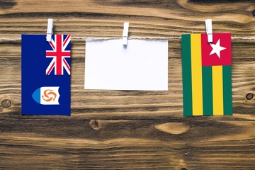 Hanging flags of Anguilla and Togo attached to rope with clothes pins with copy space on white note paper on wooden background.Diplomatic relations between countries.