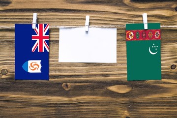 Hanging flags of Anguilla and Turkmenistan attached to rope with clothes pins with copy space on white note paper on wooden background.Diplomatic relations between countries.