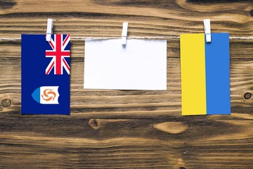 Hanging flags of Anguilla and Ukraine attached to rope with clothes pins with copy space on white note paper on wooden background.Diplomatic relations between countries.