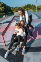 Three girls schoolgirls teenagers 13-15 years old, autumn day summer city, skateboarding. Emotions joy are fun enjoyment, happy are smiling laughing, casual clothes, relaxing after school on vacation.