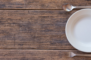 Top view of White dish and fork and spoon cutlery  on a wooden background
