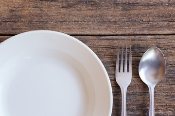 Top view of White dish and fork and spoon cutlery  on a wooden background