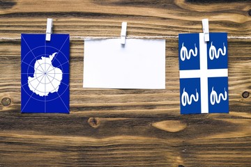 Hanging flags of Antarctica and Martinique attached to rope with clothes pins with copy space on white note paper on wooden background.Diplomatic relations between countries.