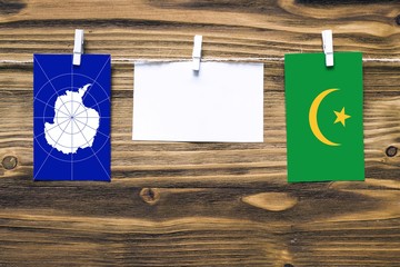 Hanging flags of Antarctica and Mauritania attached to rope with clothes pins with copy space on white note paper on wooden background.Diplomatic relations between countries.