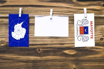 Hanging flags of Antarctica and Mayotte attached to rope with clothes pins with copy space on white note paper on wooden background.Diplomatic relations between countries.