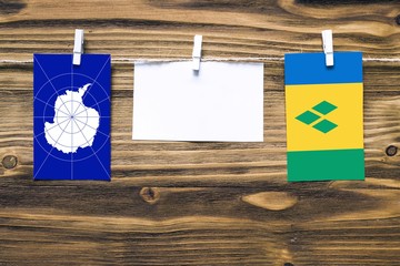 Hanging flags of Antarctica and Saint Vincent And The Grenadines attached to rope with clothes pins with copy space on white note paper on wooden background.Diplomatic relations between countries.