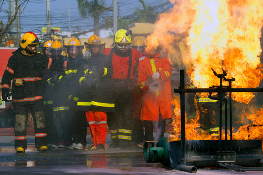   Photos Firefighter in fire fighting suit spraying water, Firemen fighting raging fire with huge flames of burning, 