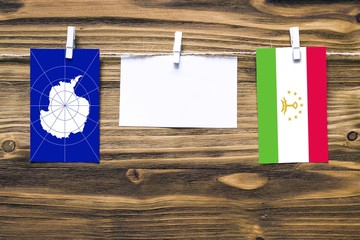 Hanging flags of Antarctica and Tajikistan attached to rope with clothes pins with copy space on white note paper on wooden background.Diplomatic relations between countries.