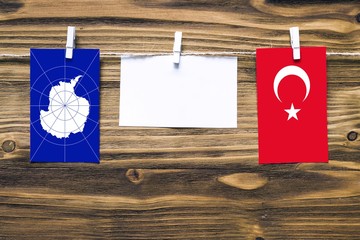 Hanging flags of Antarctica and Turkey attached to rope with clothes pins with copy space on white note paper on wooden background.Diplomatic relations between countries.