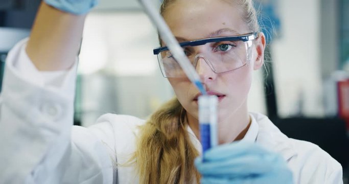 Portrait of blond female scientist is analyzing with a pipette a liquid to extract the DNA and molecules in the test tubes in laboratory. 