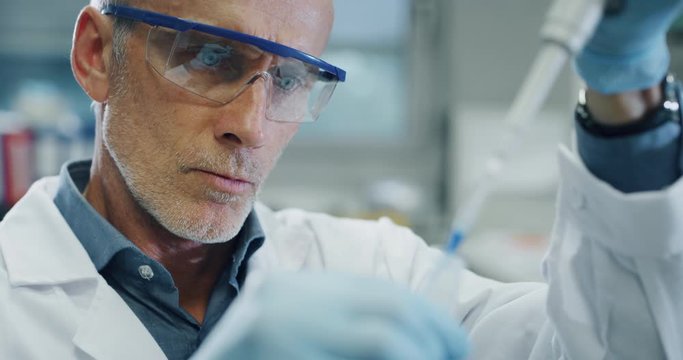 Portrait of male scientist is analyzing with a pipette a liquid to extract the DNA and molecules in the test tubes in laboratory. 