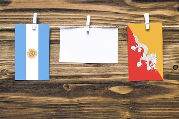 Hanging flags of Argentina and Bhutan attached to rope with clothes pins with copy space on white...