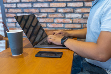 Human hand typing laptop next to coffee cup and smartphone