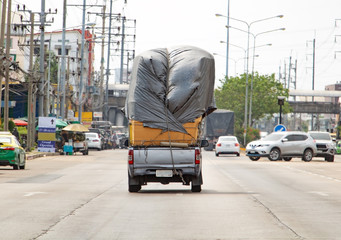 Pickup carries a many paper box on heap covered with large canvas. Car transports pile of goods on...