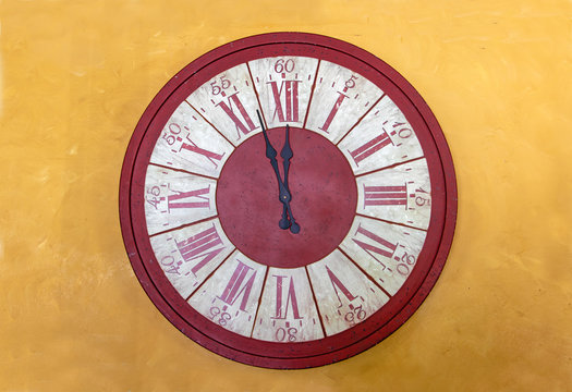 The red clock with Roman numerals shows for five minutes twelve hours. The midnight on tower clock on yellow facade.