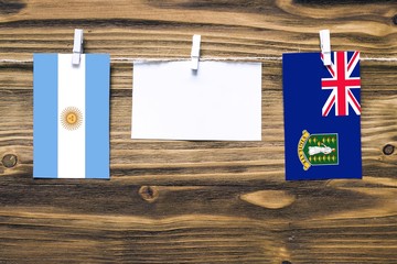 Hanging flags of Argentina and British Virgin Islands attached to rope with clothes pins with copy space on white note paper on wooden background.Diplomatic relations between countries.