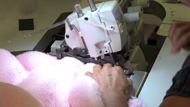 Professional seamstress serging a pink dress to prevent fraying