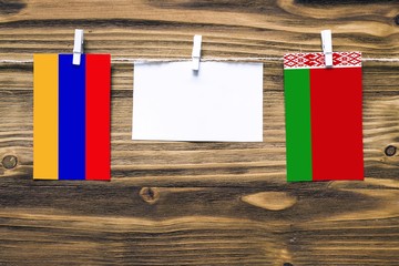 Hanging flags of Armenia and Belarus attached to rope with clothes pins with copy space on white note paper on wooden background.Diplomatic relations between countries.