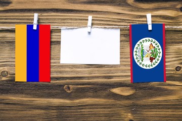 Hanging flags of Armenia and Belize attached to rope with clothes pins with copy space on white note paper on wooden background.Diplomatic relations between countries.