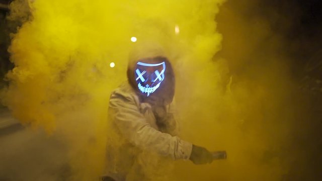 Man with purge mask and smoke grenade is dancing under a bridge at night.