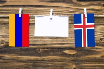 Hanging flags of Armenia and Iceland attached to rope with clothes pins with copy space on white note paper on wooden background.Diplomatic relations between countries.