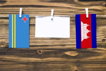 Hanging flags of Aruba and Cambodia attached to rope with clothes pins with copy space on white note paper on wooden background.Diplomatic relations between countries.