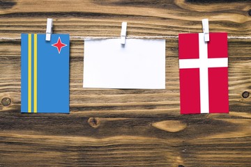 Hanging flags of Aruba and Denmark attached to rope with clothes pins with copy space on white note paper on wooden background.Diplomatic relations between countries.