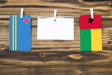 Hanging flags of Aruba and Guinea Bissau attached to rope with clothes pins with copy space on white note paper on wooden background.Diplomatic relations between countries.