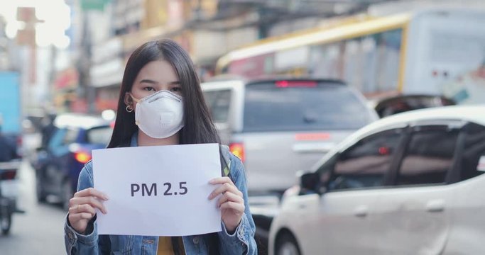 Young woman in protective mask holding pm 2.5 sign at city.