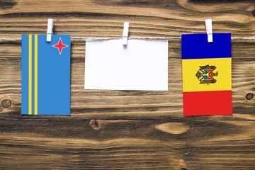 Hanging flags of Aruba and Moldova attached to rope with clothes pins with copy space on white note paper on wooden background.Diplomatic relations between countries.